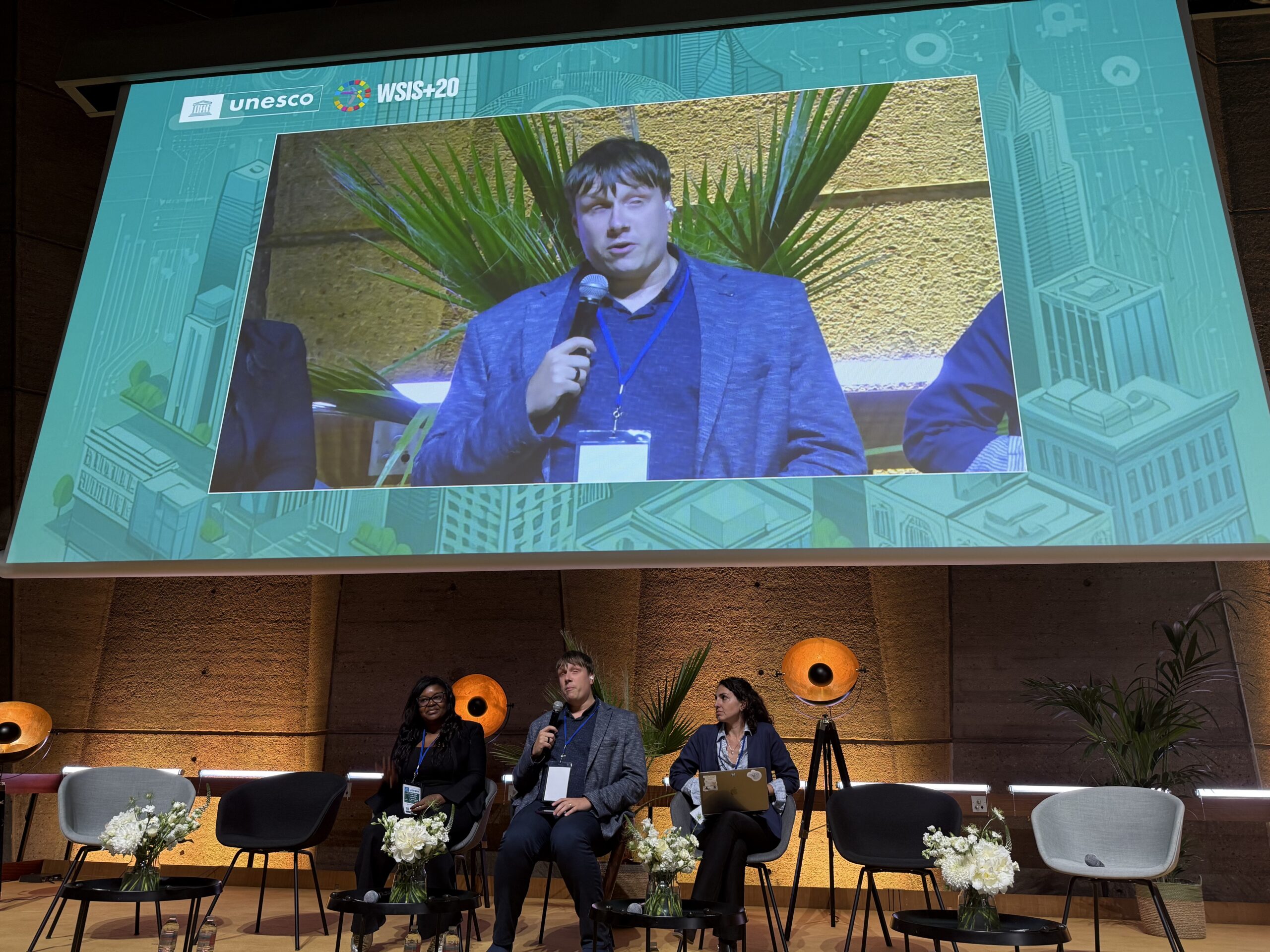 Kolm panelisti laval, jakob keskel, tema kõrval kaks naisterahvast. Taustal palmipuud. Lava kohal on ekraan, kus näidatakse samuti jakobit. Ekraani ülaosas kiri unesco”